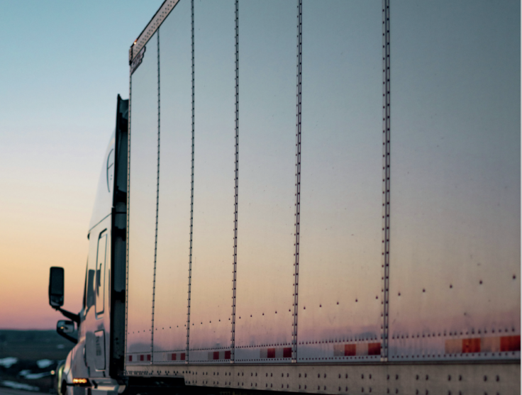White semi-truck trailer at sunset, riveted metal panels along the side with the cab visible on the left