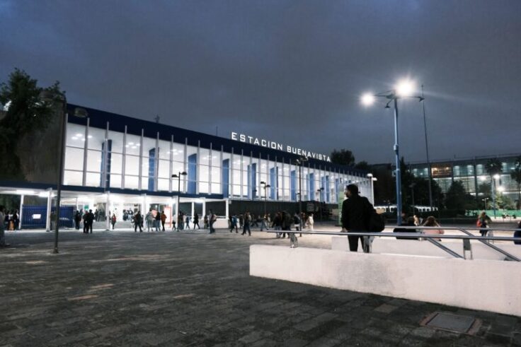 Exterior view of Estación Buenavista at dusk with a modern glass facade and people gathered in the plaza outside the station.