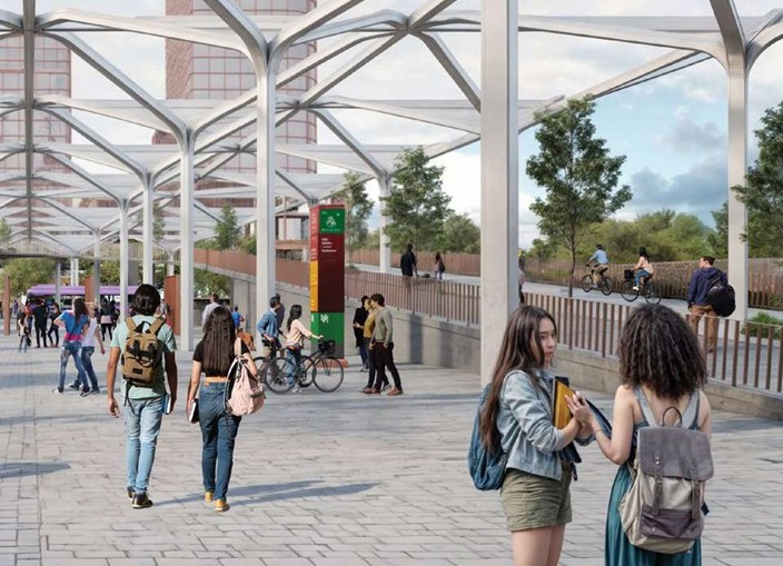 Public pedestrian plaza under a geometric steel arch canopy with people walking, cycling, and chatting near a green sign and trees in the background.