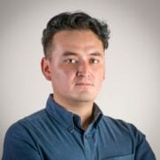 Portrait of a man with short dark hair wearing a blue button-down shirt, looking at the camera against a neutral backdrop.