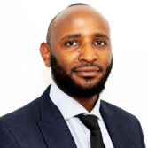 Professional headshot of a bald man with a beard in a navy suit and white shirt on a white background.