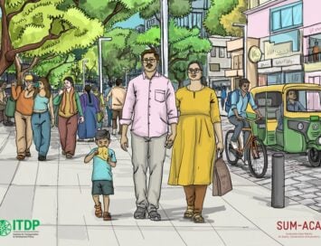 A busy urban sidewalk with a couple and their child foreground, surrounded by pedestrians; a cyclist and an auto rickshaw on a tree-lined street with shops in the background.