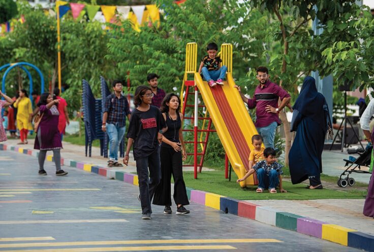 People at a colorful playground: two women walking in foreground as kids play on a yellow slide nearby.