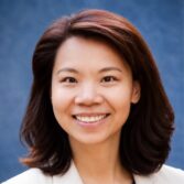 Smiling Asian woman with shoulder-length dark hair against a blue background (portrait).