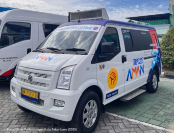White electric van with blue accents and 'Angkutan Listrik' branding parked beside another white van; license plate BM 7393 JU visible.